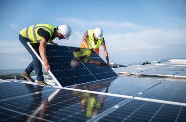 Team Of Two Engineers Installing Solar Panels On Roof.